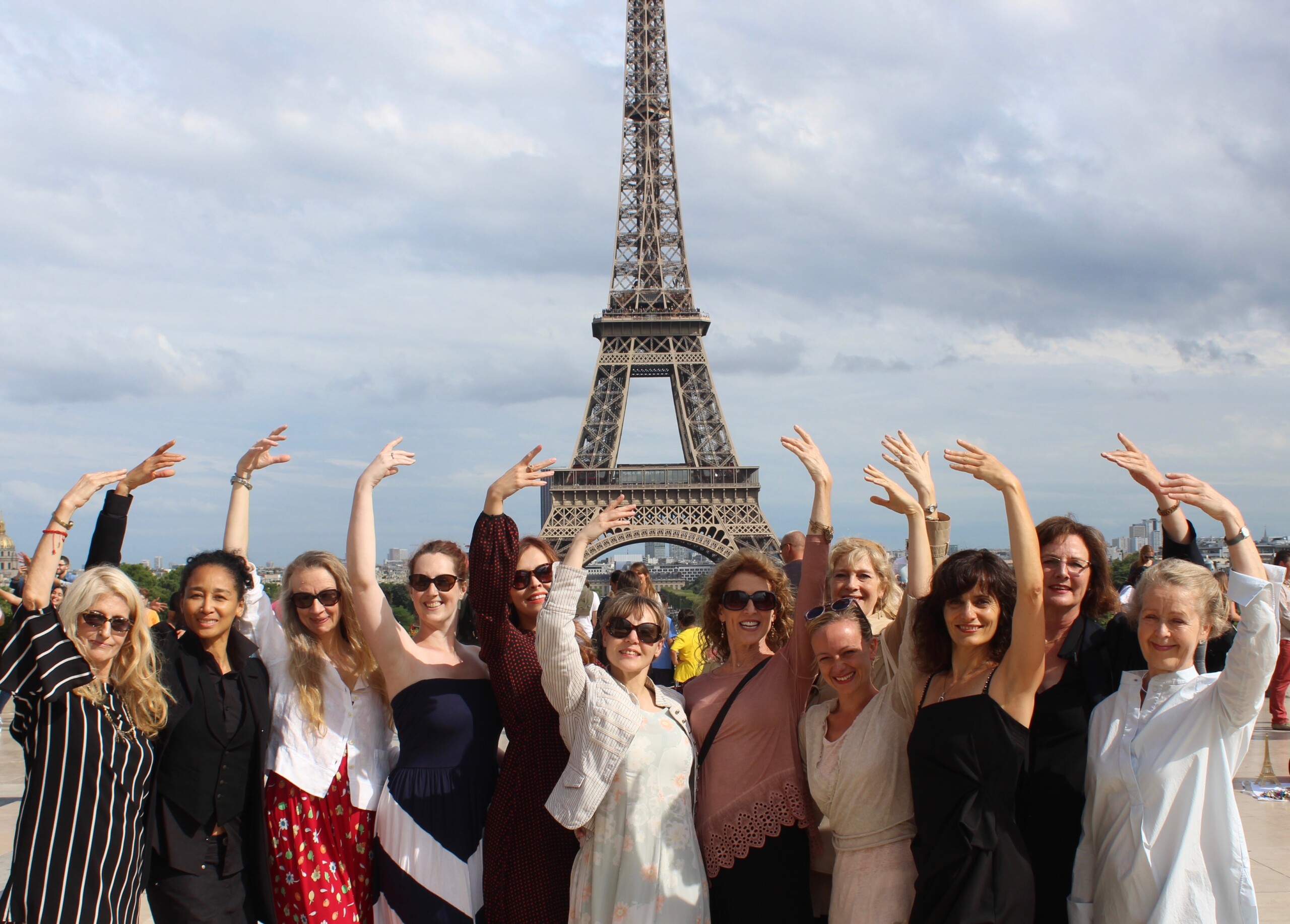 a group of women with their hands raised, the Eiffel tower behind them